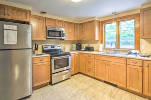 A modern kitchen with wooden cabinets, stainless steel appliances, and a large window providing natural light.