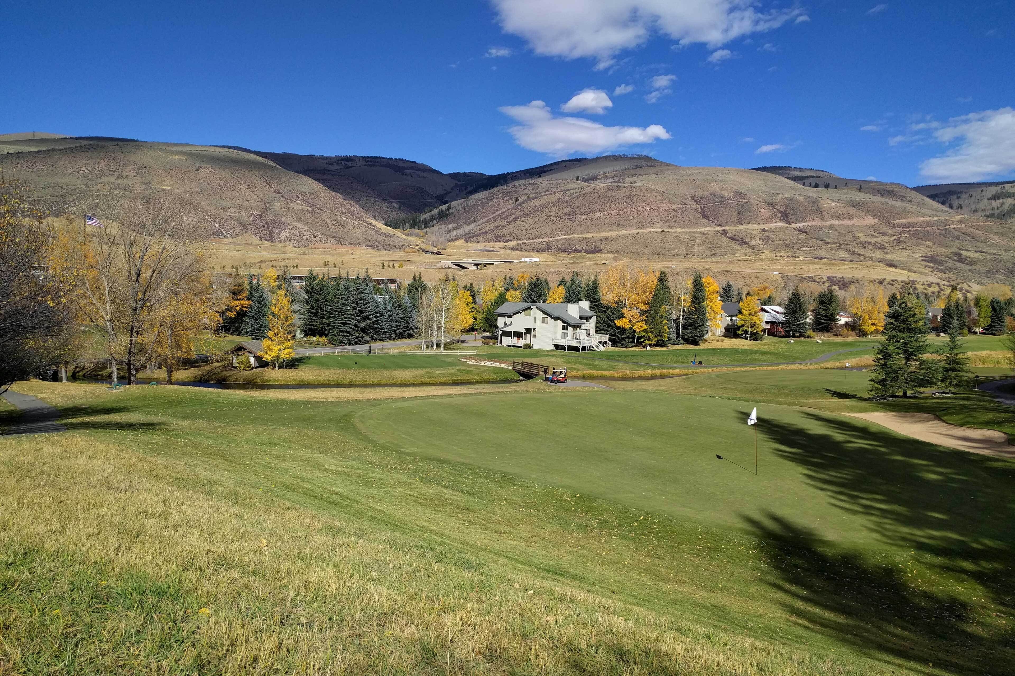 Un campo de golf con un club de campo, rodeado de árboles de colores otoñales y montañas.