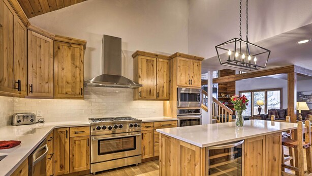 Una cocina con armarios de madera, una isla central, electrodomésticos de acero inoxidable y una lámpara colgante.