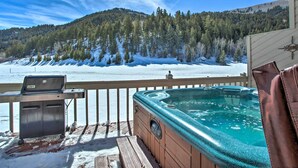 Un jacuzzi en una terraza de madera con vistas a un paisaje nevado y una parrilla.