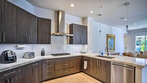 Une cuisine moderne avec des meubles de couleur bois foncé, des appareils en acier inoxydable et un plan de travail de couleur claire.