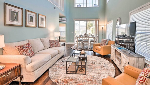 A spacious living room with a high ceiling, a ceiling fan, a dining area with a table and chairs, and a television on a wooden cabinet. - Golfers Paradise in Myrtle Beach w/ Balcony! (Myrtle Beach)