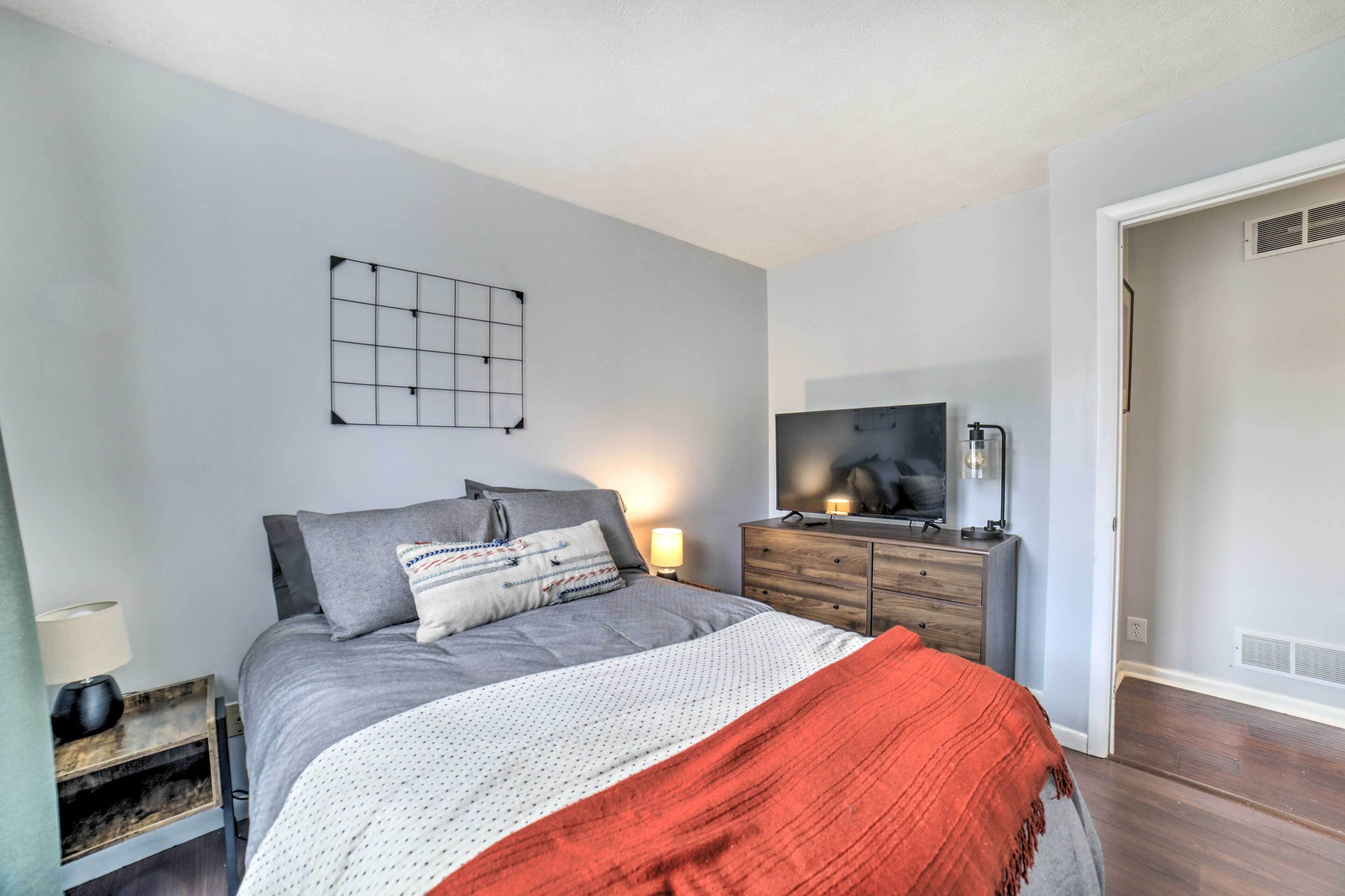 A bedroom with a bed, a dresser, a TV, and a wall-mounted light fixture.