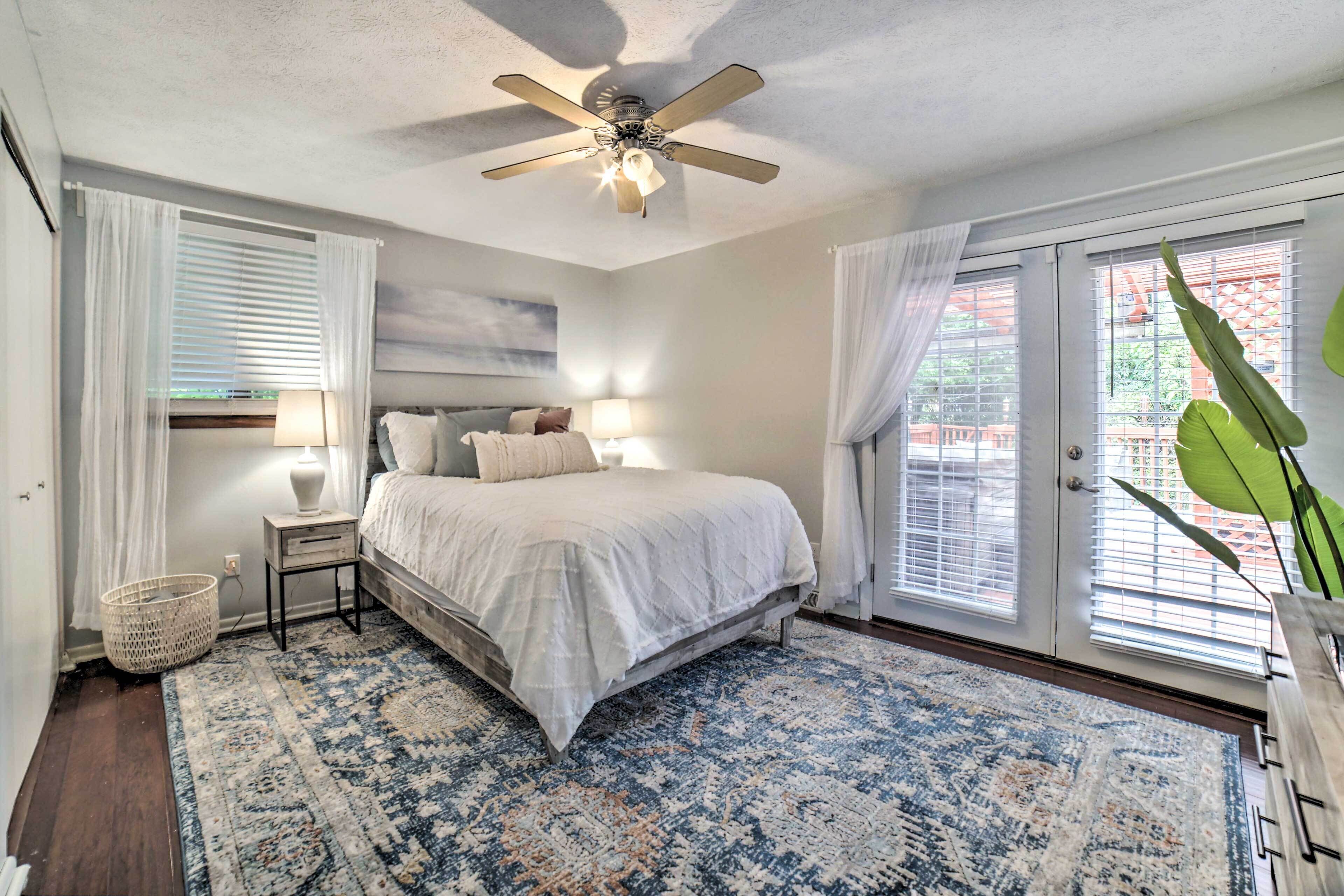 A bedroom with a bed, bedside tables, a ceiling fan, and a large window with blinds.