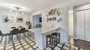 A modern kitchen with a central island, black bar stools, and a dining area with a checkered floor. - Pittsburgh Retreat w/ Deck ~ 4 Mi to Dtwn! (Pittsburgh)