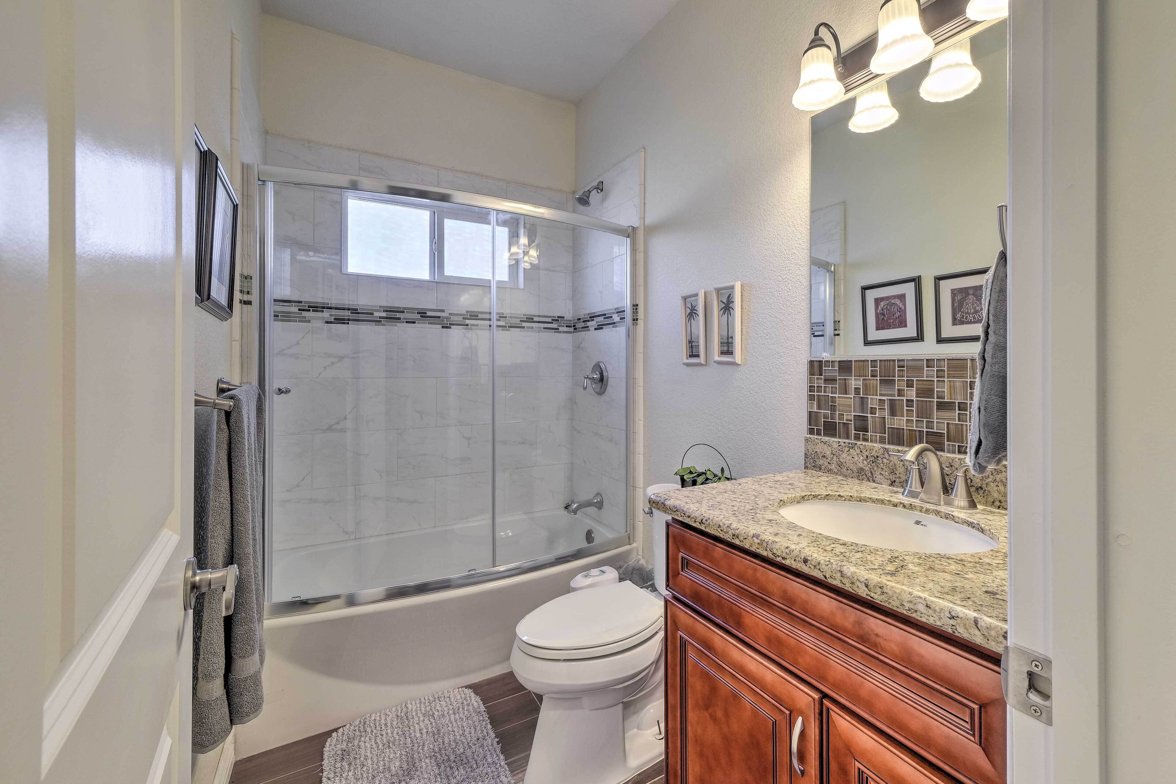 A bathroom with a glass-enclosed shower, a white toilet, a granite countertop sink, wooden cabinets, and framed pictures on the wall.