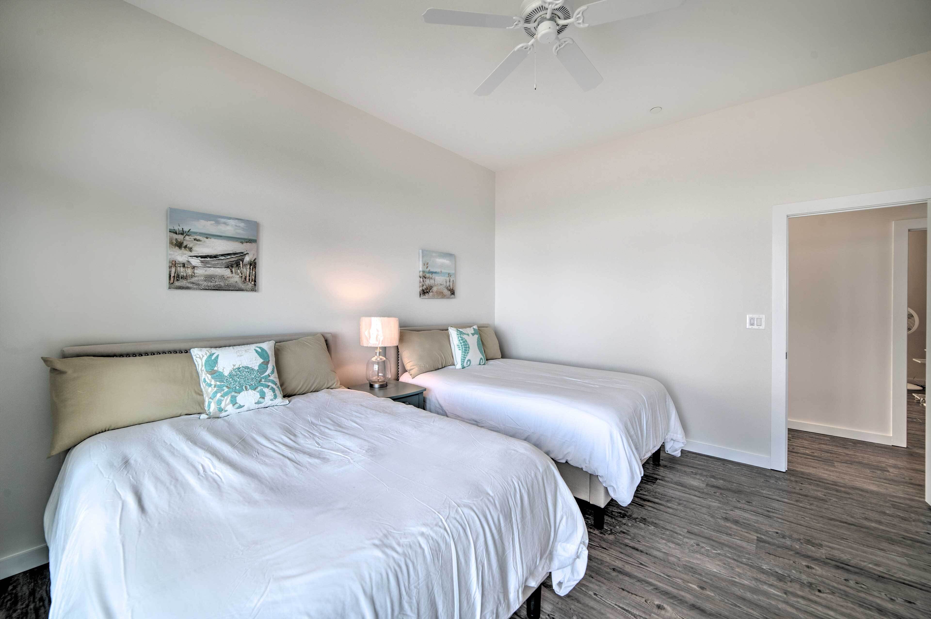 A hotel room with two beds, a ceiling fan, and two wall-mounted paintings.