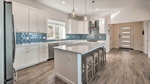 A modern kitchen with white cabinets, a large island with bar stools, and blue-tiled backsplash. - Waterfront Scotland Beach Retreat w/ Private Beach (Ridge)
