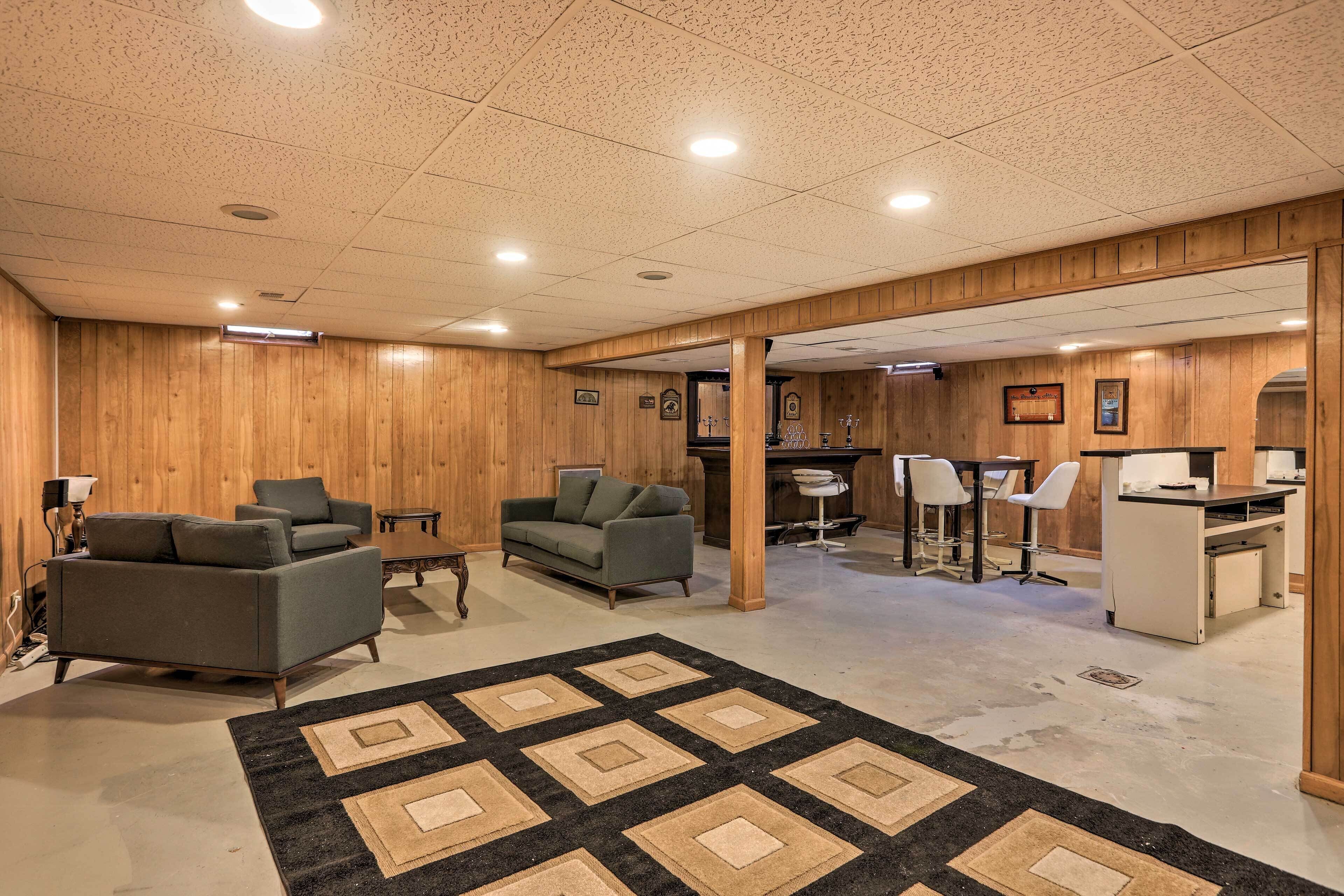 Une pièce spacieuse aux murs en bois, avec un grand tapis, deux canapés, un bureau et un coin bar.