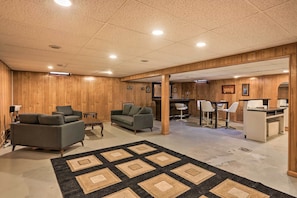 Une pièce spacieuse aux murs en bois, avec un grand tapis, deux canapés, un bureau et un coin bar.