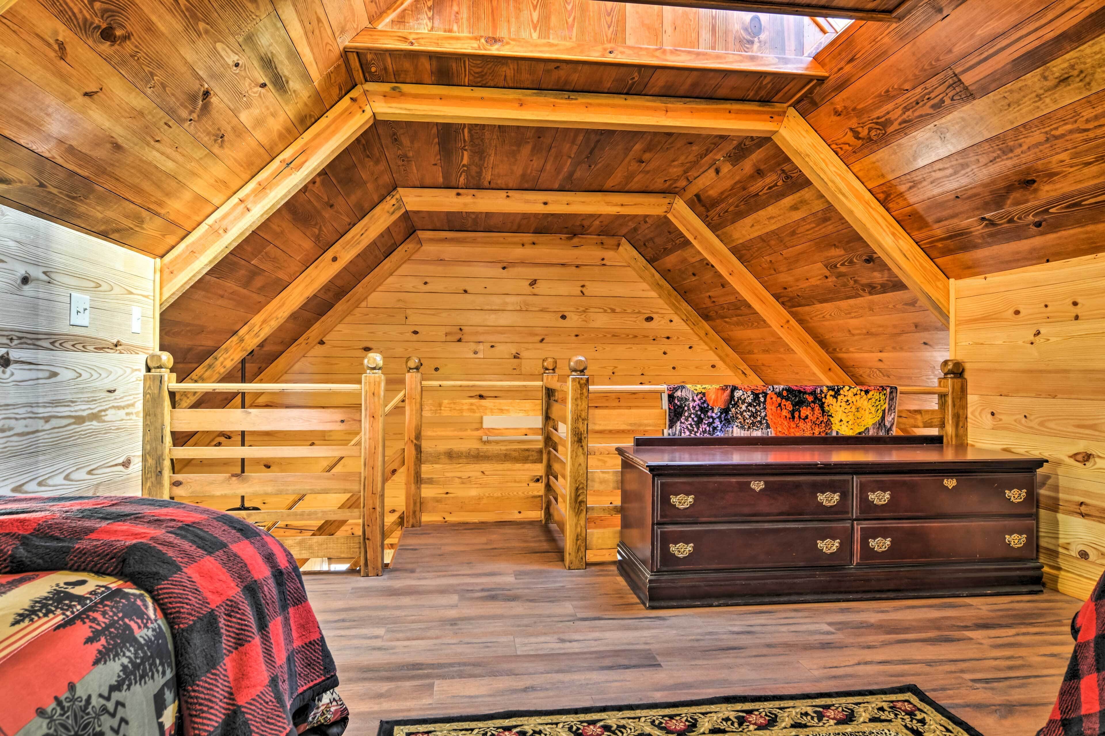A cozy attic bedroom with wooden walls and a sloped ceiling, featuring a bed, dresser, and a small window.