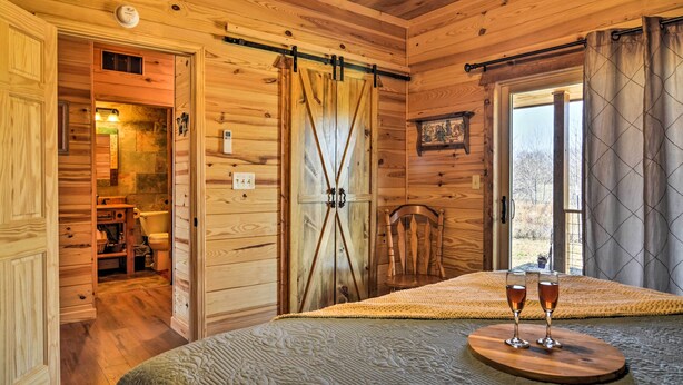 Quarto de cabana de madeira com cama, poltrona, porta deslizante e janela com cortinas.