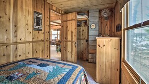 Ein gemütliches Holzblockhaus-Interieur mit gesteppter Bettdecke, einem Ventilator und Blick durch ein Fenster.