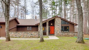 A rustic cabin with a stone facade, wooden siding, and a prominent red door. - Game Room! Mid-century Escape in the Northwoods (Woodruff)