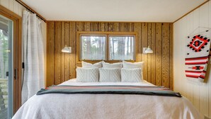 A bedroom with a bed, two bedside lamps, a window, and a wall-mounted blanket. - Game Room! Mid-century Escape in the Northwoods (Woodruff)