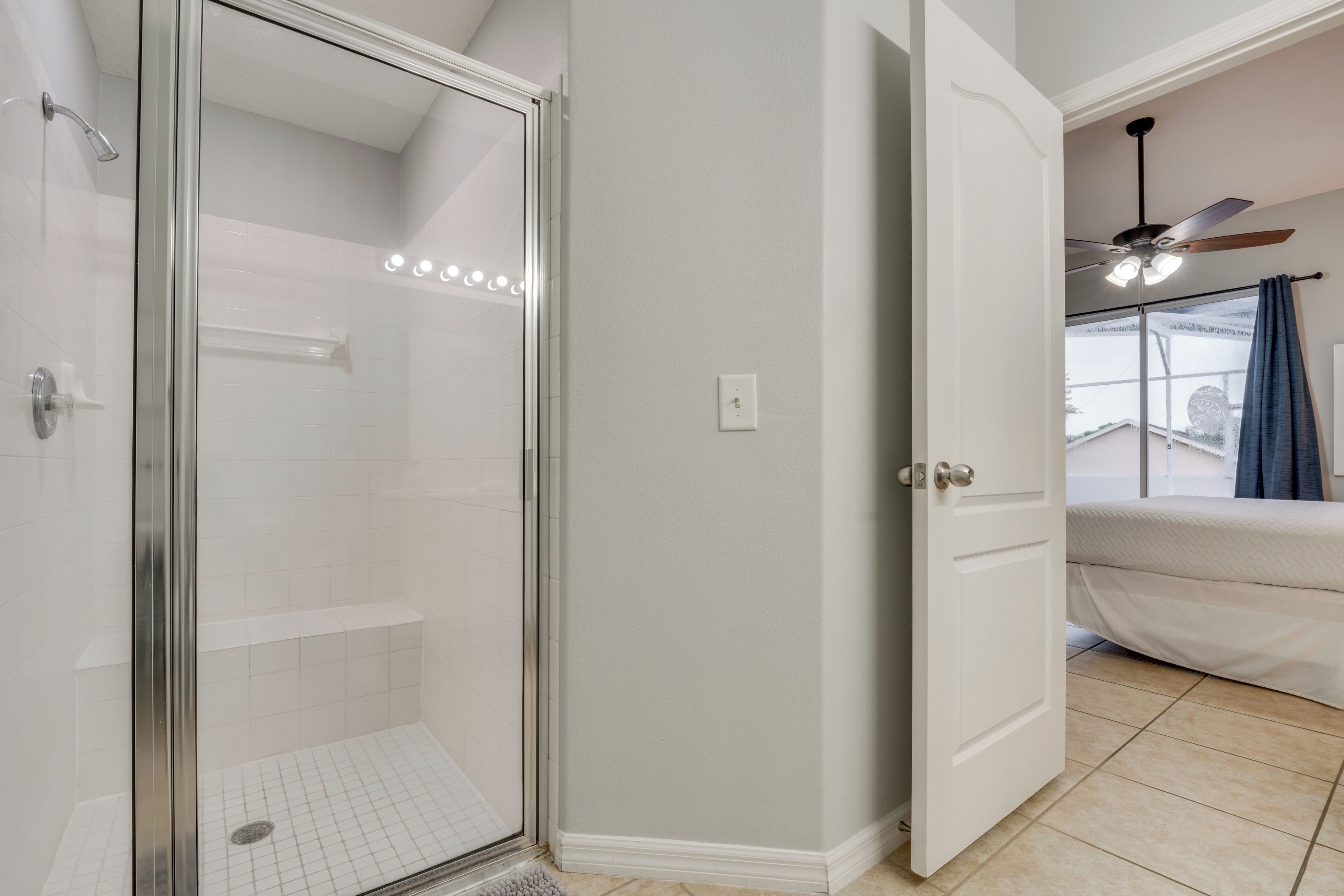 A bathroom with a glass-enclosed shower, a white door, and a ceiling fan.