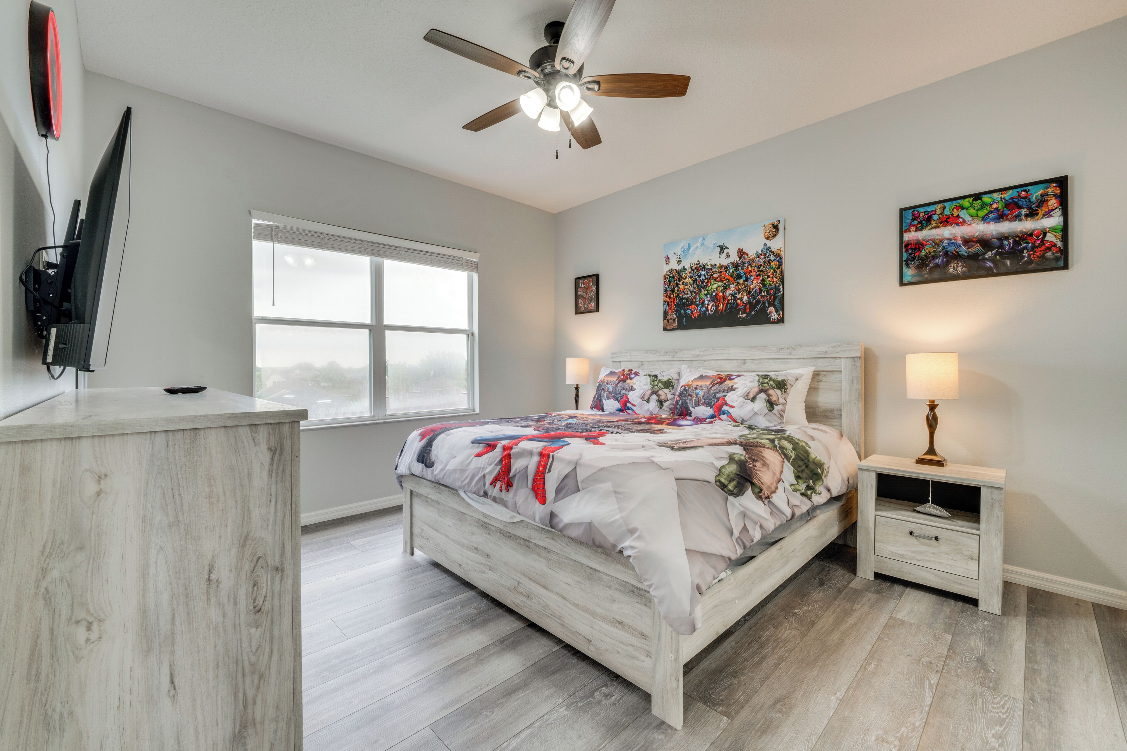 A bedroom with a bed, a nightstand, a ceiling fan, a window, and artwork on the walls.
