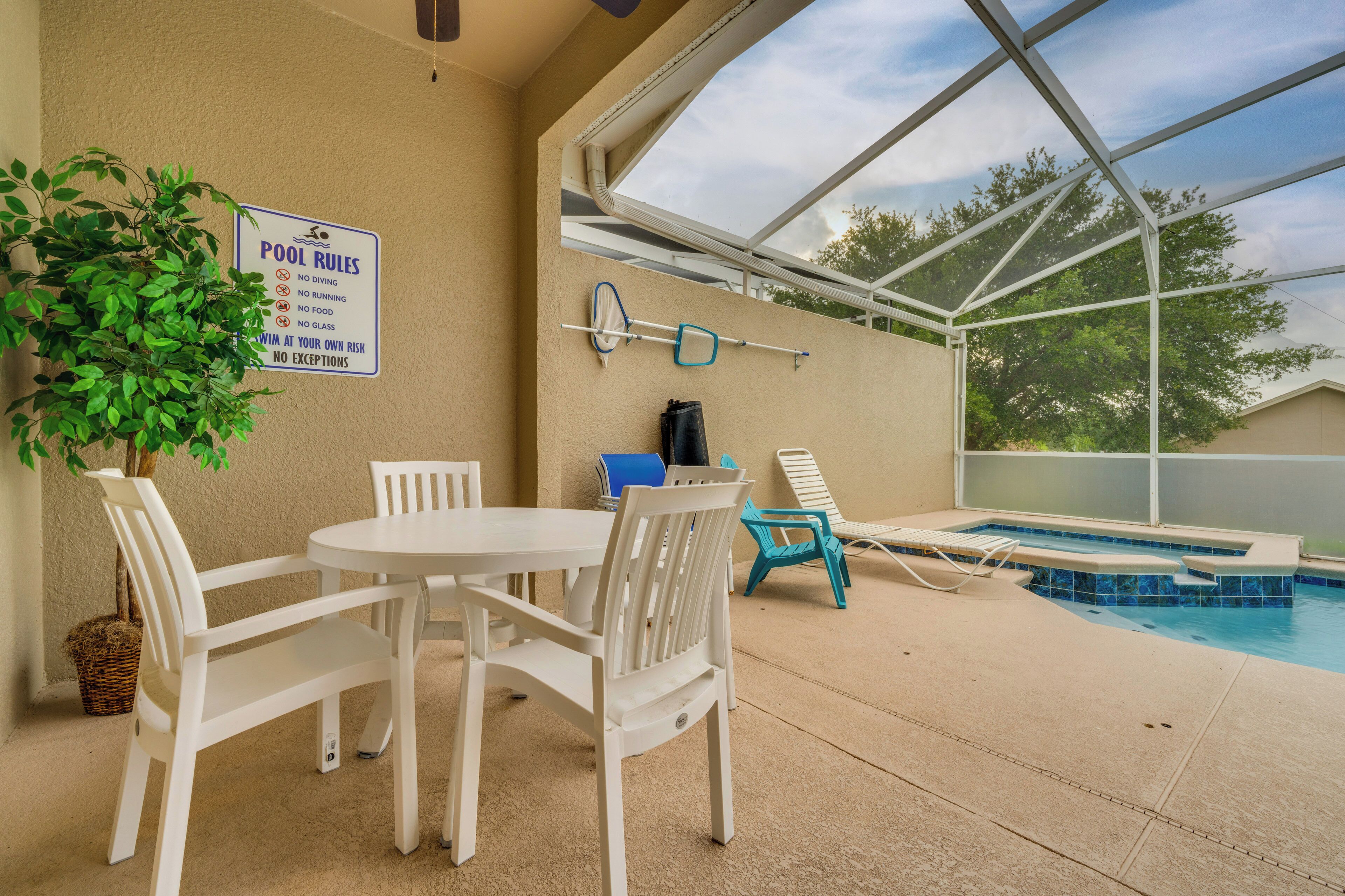 An indoor pool area with a table and chairs, a sign listing pool rules, and a view through a glass enclosure.
