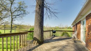 Eine Holzterrasse mit einem Ziegelgebäude, einem Baum und einem grasbewachsen Feld im Hintergrund.