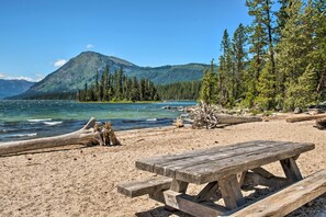 A beach with a wooden picnic table, clear blue water, and a mountain in the background. - Koul's Retreat' Condo 2 Mi to Lake Wenatchee (Leavenworth)
