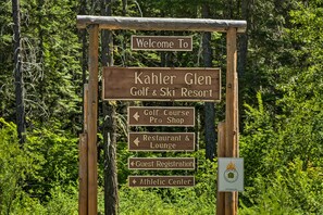 A wooden signpost with multiple directional arrows indicating various facilities at the Kahler Glen Golf & Ski Resort, including a Golf Course Pro Shop, Restaurant & Lounge, Guest Registration, and Athletic Center. - Koul's Retreat' Condo 2 Mi to Lake Wenatchee (Leavenworth)