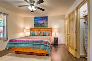 A bedroom with a wooden bed, two bedside lamps, a ceiling fan, a night sky painting, and a wooden wardrobe.