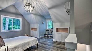 A bedroom with a large bed, a desk, and a chair, a small kitchen area, and a view of the outdoors.