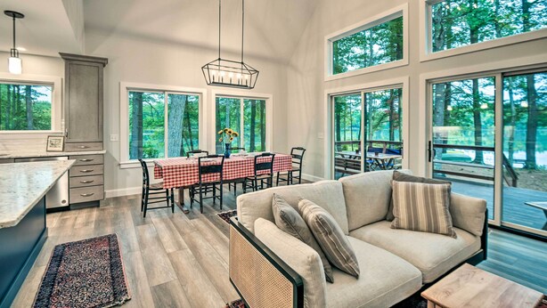 A spacious living area with a large window, a dining table with chairs, and a sofa with pillows.