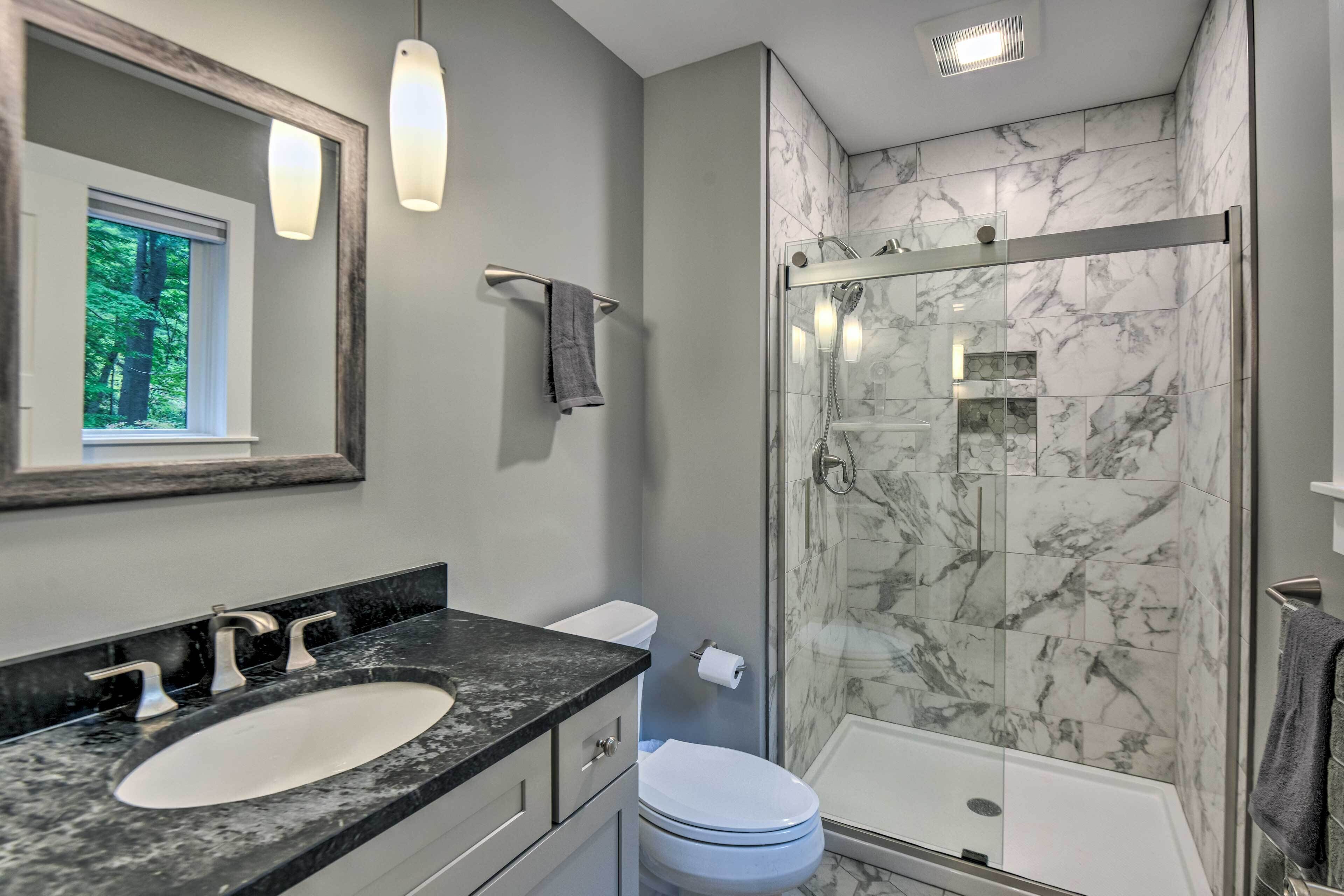 A modern bathroom with a marble shower, a sink with a marble countertop, and a toilet.