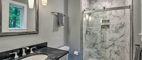 A modern bathroom with a marble shower, a sink with a marble countertop, and a toilet.