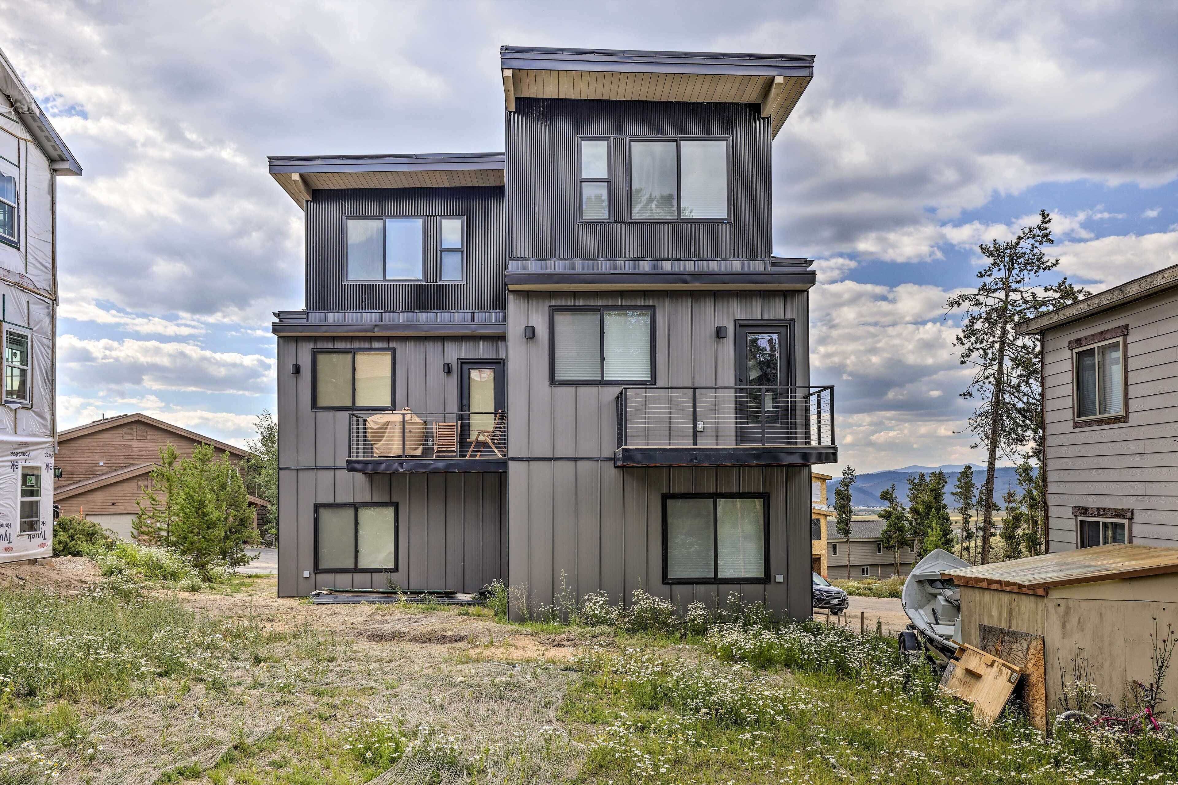 A modern two-story house with a balcony, large windows, and a view of the surrounding landscape.