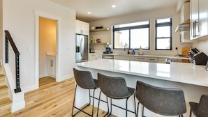 A modern kitchen with a large island, bar stools, stainless steel appliances, and ample natural light from large windows. - Sleek Fraser Townhome < 8 Mi to Winter Park! (Fraser)