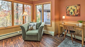 Una habitación acogedora con un sillón verde, un escritorio de madera y grandes ventanales con vistas a un bosque.
