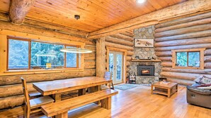 A log cabin interior with a wooden dining table, benches, a fireplace, and large windows. - Riverfront Gold Bar Log Cabin Near Stevens Pass! (Gold Bar)