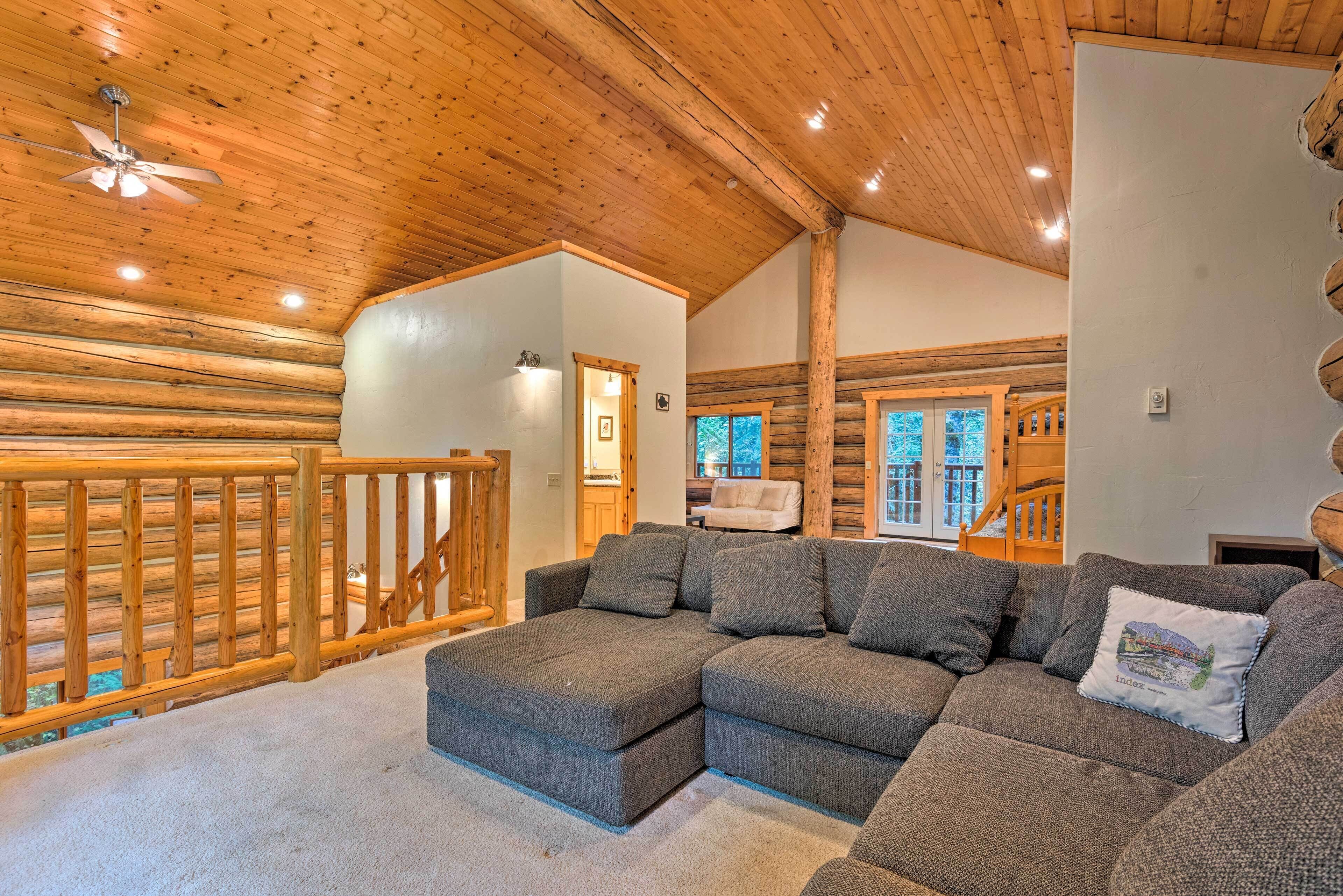 Ein Holzblockhaus-Interieur mit einem Ecksofa, Holzgeländer und einem Deckenventilator.