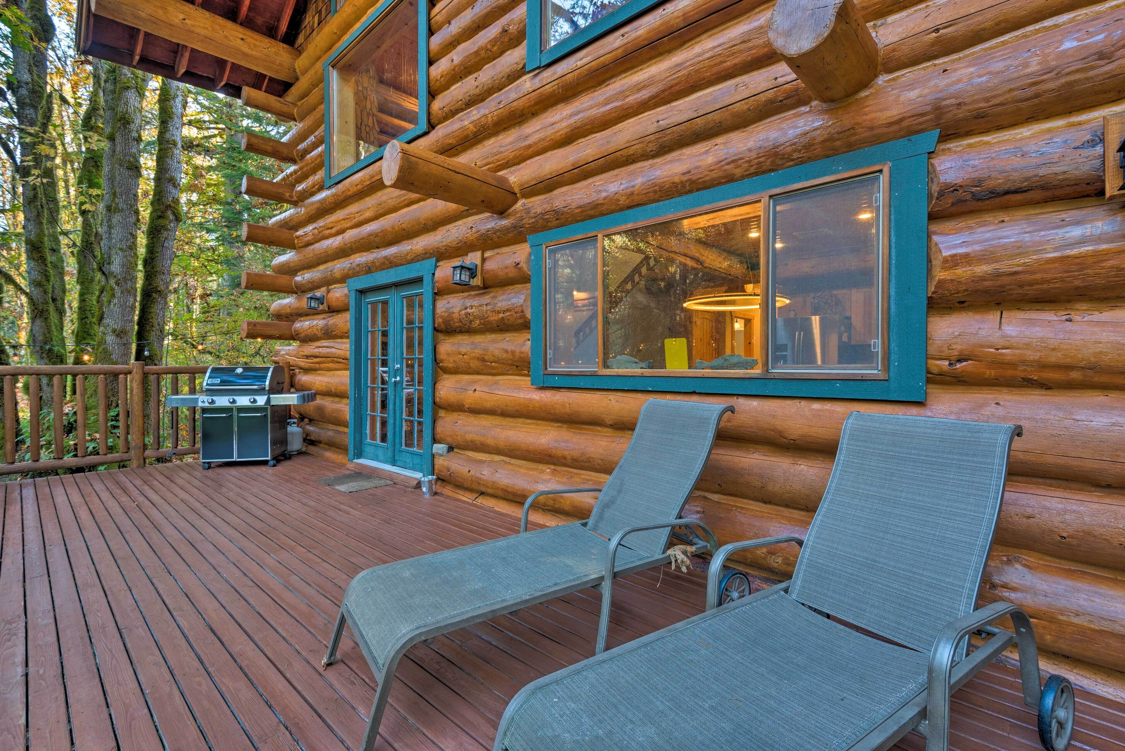 Une cabane en rondins avec une terrasse, deux chaises longues, un barbecue et une fenêtre donnant sur la forêt.