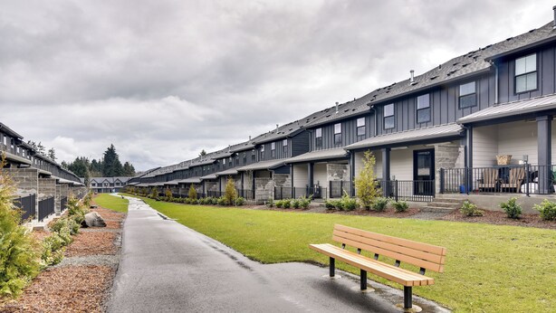 En rad moderna radhus med en stenlagd gångväg och en bänk.