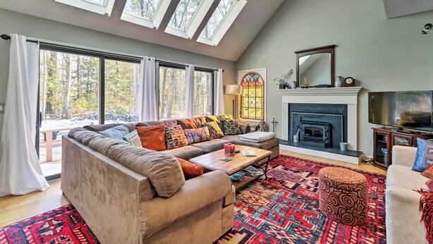 A spacious living room with a large sofa, a fireplace, a television, and a skylight. - Peaceful Goshen Cottage w/ Screened Porch & Views! (Goshen)