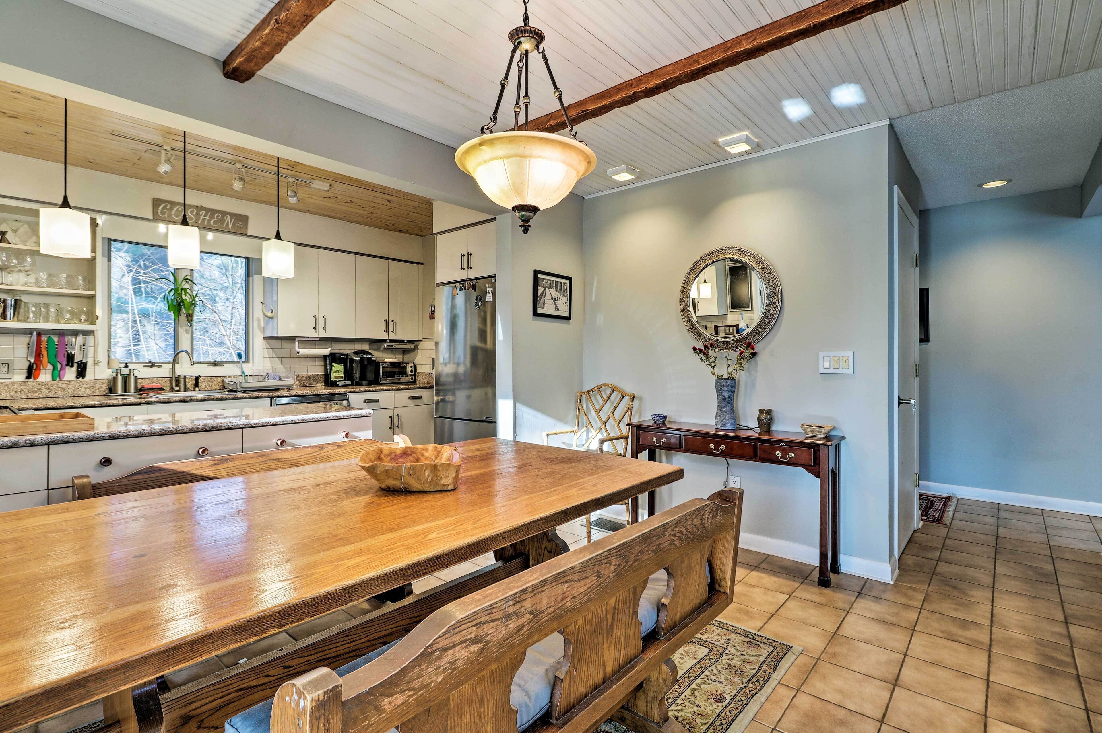 A spacious kitchen with wooden cabinets, a large wooden dining table, and a hanging light fixture.