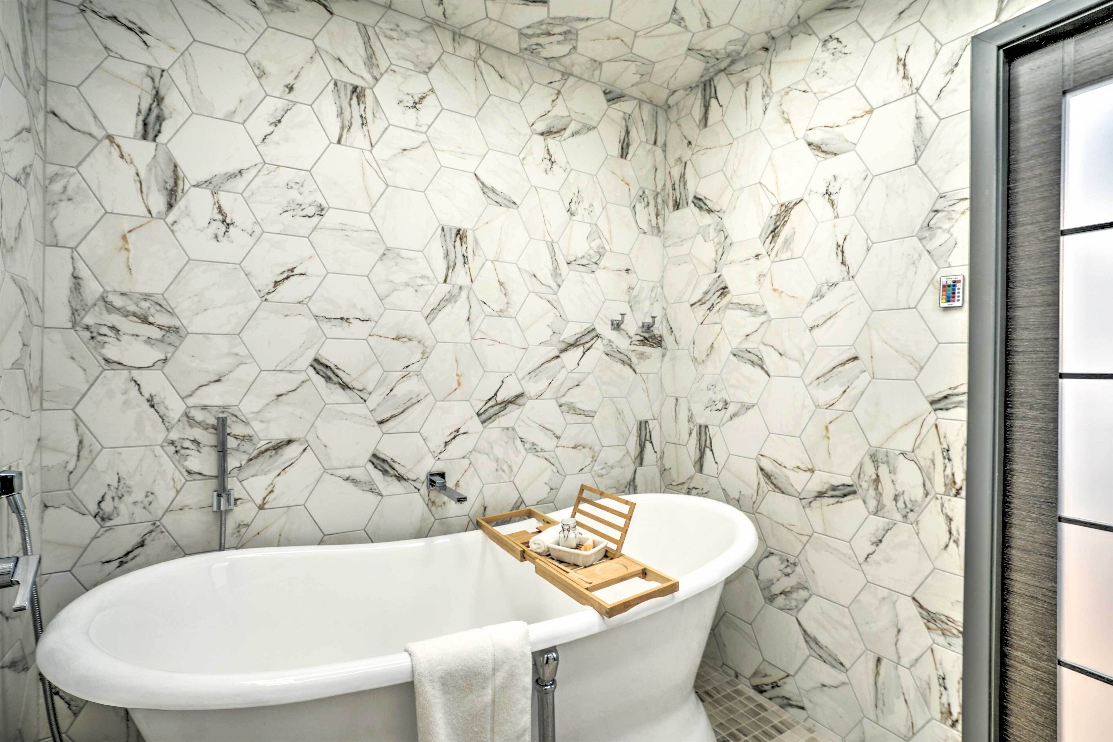 A bathroom with a freestanding bathtub, marble hexagonal tiles, and a wooden tray with toiletries.