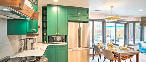 A modern kitchen with green cabinets, stainless steel appliances, and a dining area with a wooden table and chairs.