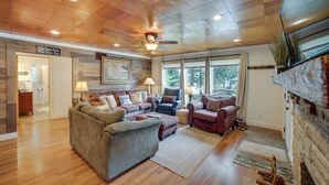 A spacious living room with a wooden ceiling, a fireplace, and large windows. - Waterfront Monticello Home w/ Fire Pit & Deck! (Monticello)