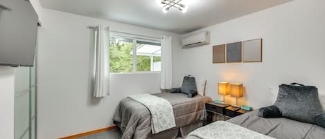 A hotel room with two beds, a desk with a lamp, an air conditioner, and a window with curtains.