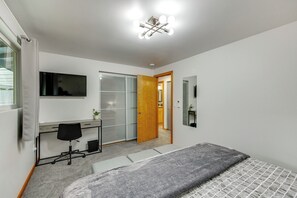 A bedroom with a bed, a desk with a chair, a TV, a sliding door, and a mirror. - Redmond Retreat w/ Fenced Yard & EV Charger (Redmond)