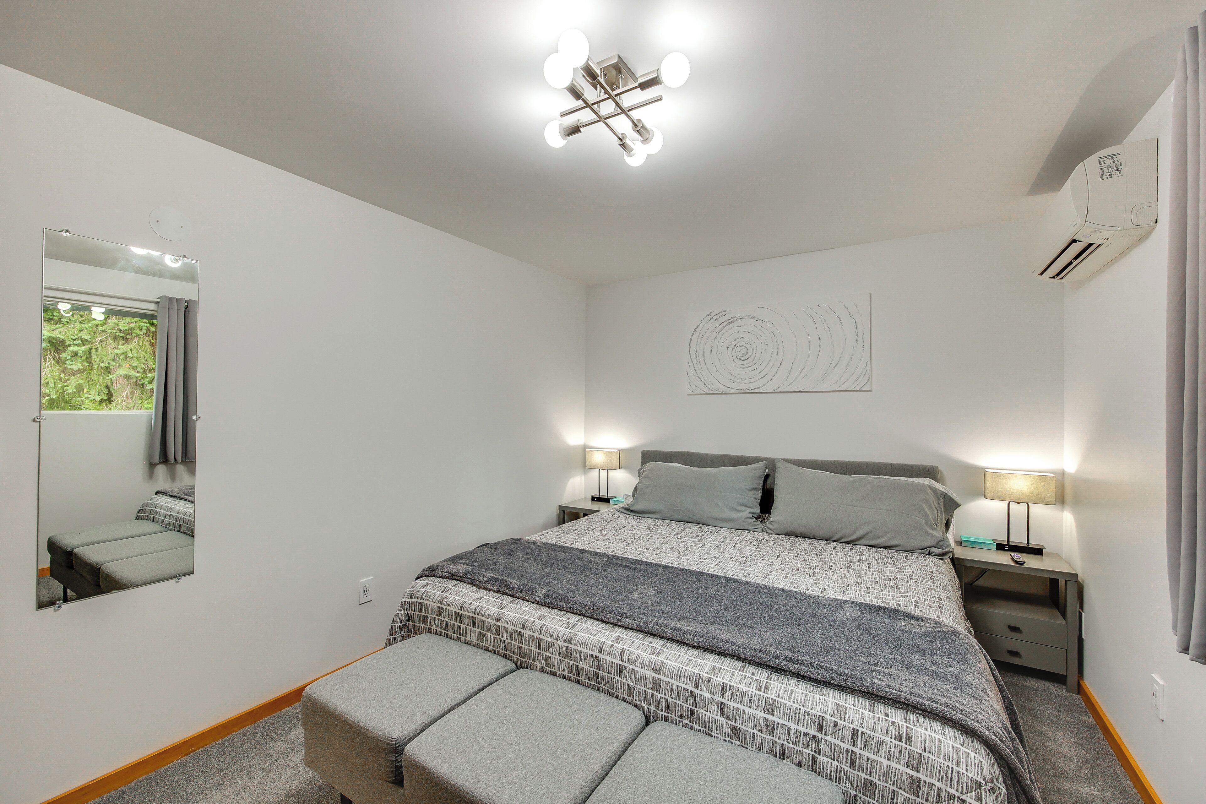 Une chambre à coucher avec un lit, des lampes de chevet, un miroir, un tableau décoratif au mur et une fenêtre avec des rideaux.