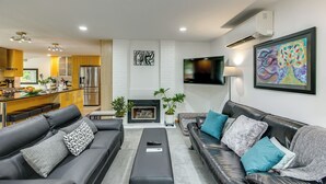 A modern living room with a fireplace, a kitchen in the background, and a flat-screen TV mounted on the wall. - Redmond Retreat w/ Fenced Yard & EV Charger (Redmond)