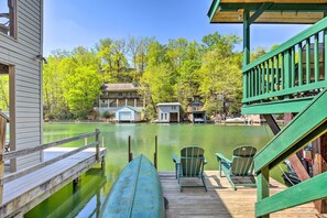 A wooden dock with a canoe, two green Adirondack chairs, and a view of a lake with buildings in the background. - Screened Porch & Grill: Waterfront Landrum Cottage (Landrum)