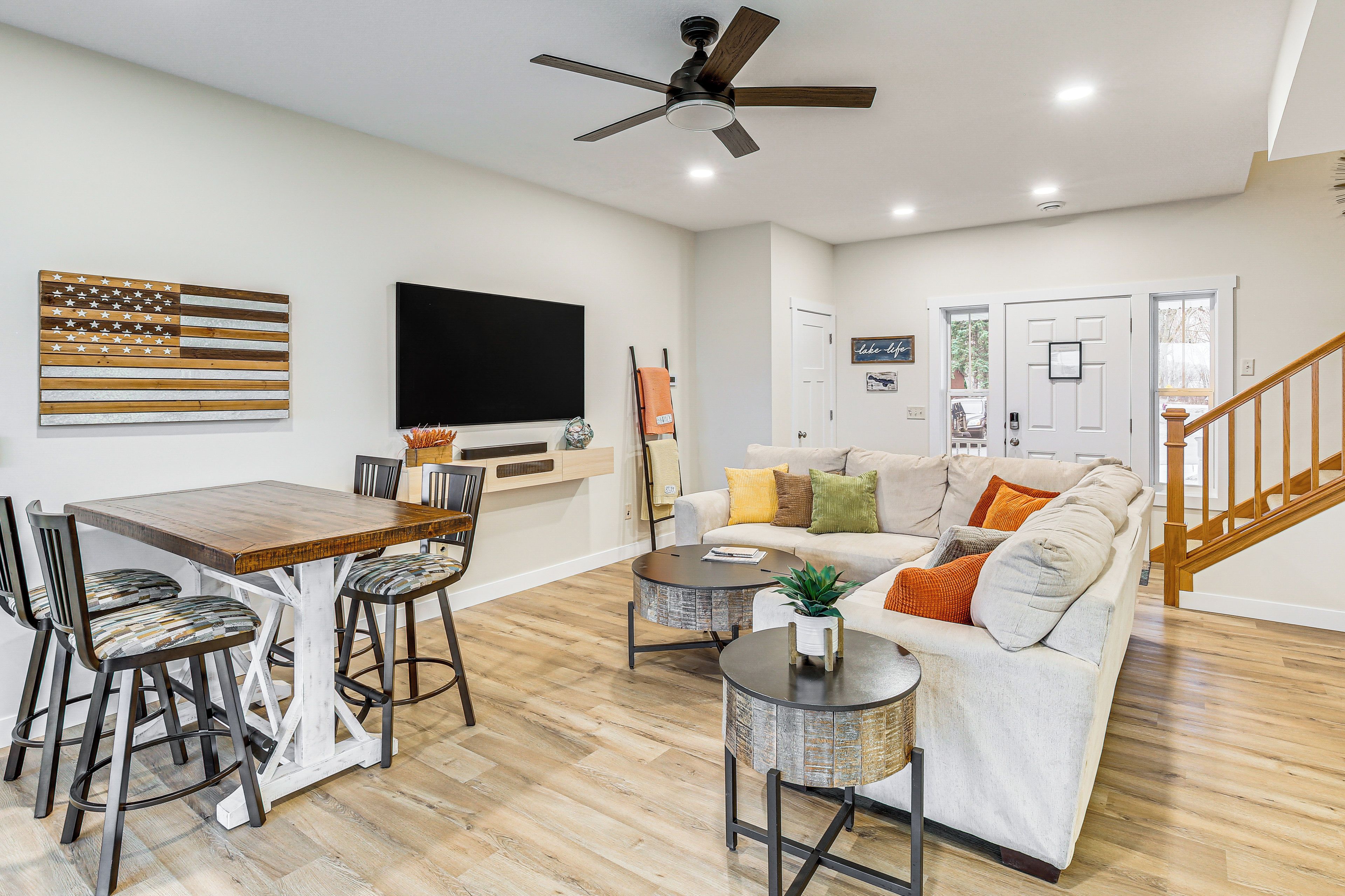 A living room with a wooden dining table, bar stools, a sofa, a coffee table, and a ceiling fan.