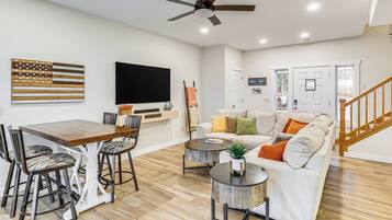 A living room with a wooden dining table, bar stools, a sofa, a coffee table, and a ceiling fan.