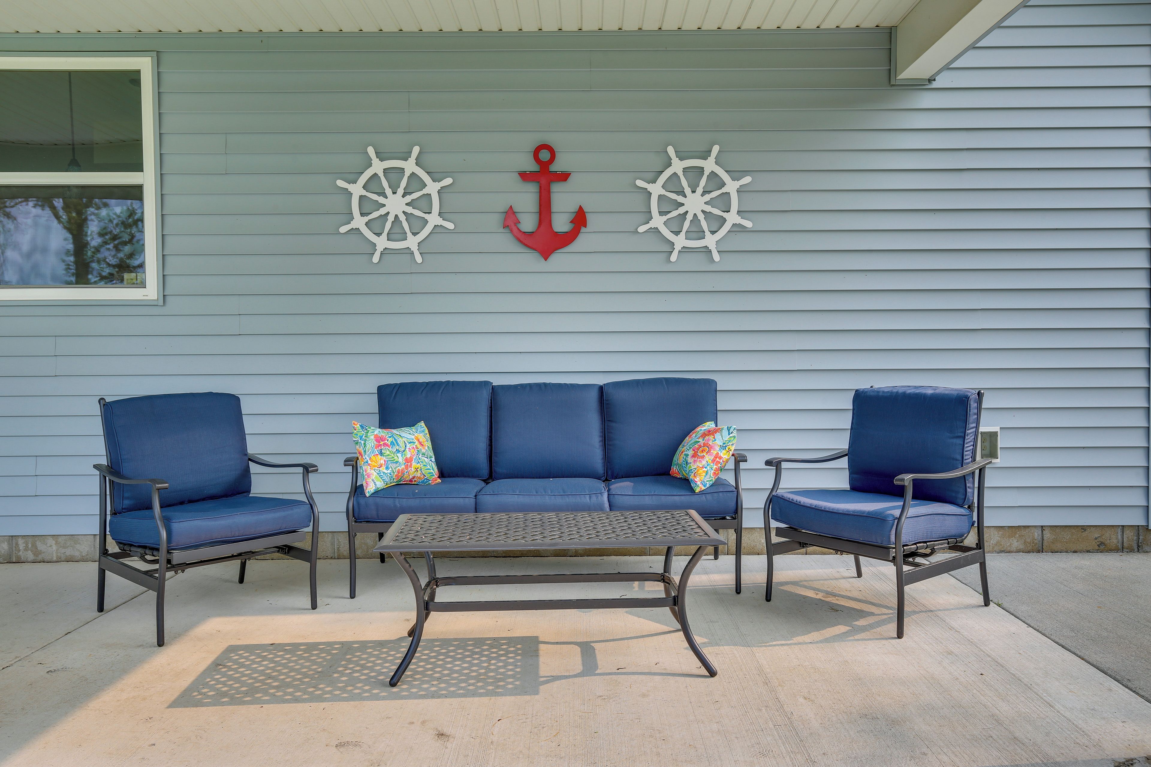 A blue outdoor seating area with a metal table and two blue chairs, a red anchor, and two ship wheels on the wall.